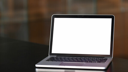 Fototapeta premium An open mock up laptop computer with blank white screen on black wooden table at conference room.