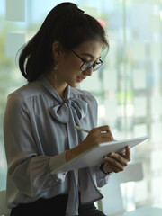 Businesswoman working with digital tablet while standing in glass partition office room