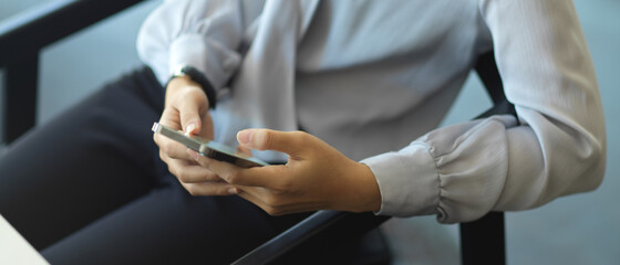 Female hands using smartphone while sitting on the chair in office room