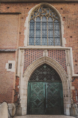 Obraz premium Amazing big old arched two-leaf emerald metal door with a beautiful window under a semicircular arch of stone. The entrance to the ancient building with orange brick wall in Krakow.