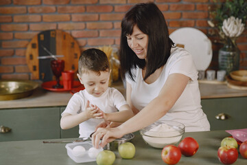 Fototapeta premium Family in a kitchen. Beautiful mother with little son. Little boy playing wit a dough.