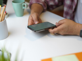 Businessman hand using smartphone on worktable with supplies in office room