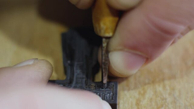 an artisan carves a carving on a wooden cross. macro shooting. A woodcarver cuts an Orthodox ebony cross with a chisel.