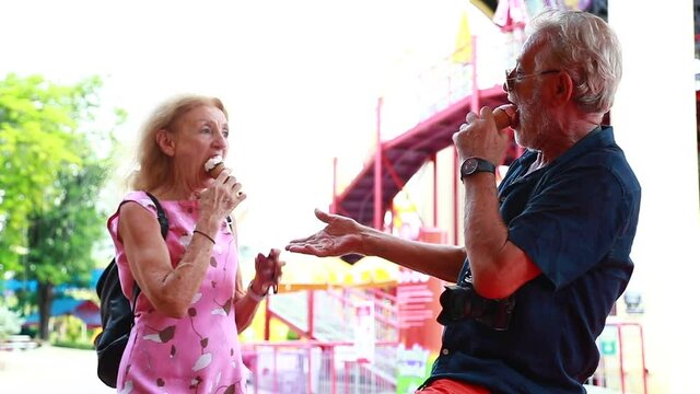 Eat ice cream cone. Happy Elderly cacasian couple dance and eat ice cream at  amusement park. Summer travel trip. Slow motion video.