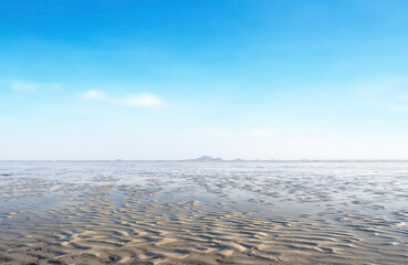 Background pattern of wavy mud on the beach during blurred low tide with blue sky and white cloud