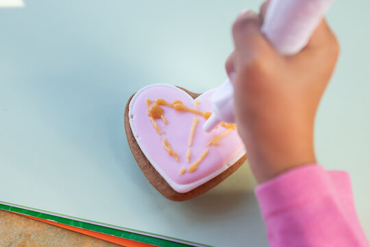 Decorating a sweet gingerbread in shape of heart. Close-up of painting different shapes of cookies using icing bag with sugar frosting on table.Child is decorating cookie.Copy space