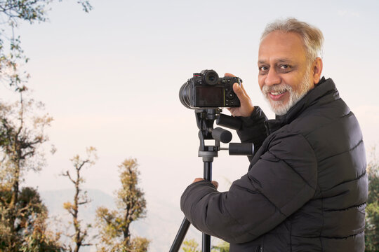 A SENIOR ADULT MAN HAPPILY LOOKING BEHIND WHILE CLICKING PICTURES ON HIS CAMERA	