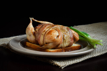 Baked quail stuffed with liver wrapped in bacon on crispy bread toast.