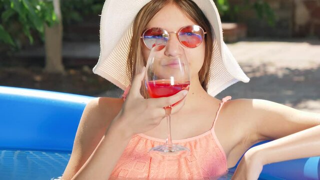 Portrait of beautiful msiling yougn girl drinking cocktail while relaxing in swimming pool at hot summer day. Concept of happy summer holidays and vacation