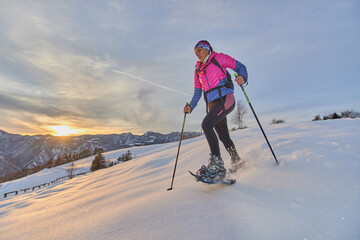 Fototapeta na wymiar Landscape at sunset in the mountains with girl running downhill with snowshoes