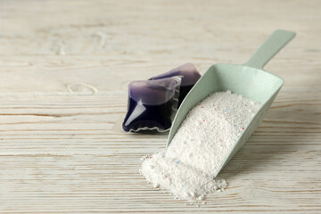 Scoop with washing powder and laundry capsules on white wooden background