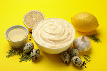 Bowl with mayonnaise and ingredients on yellow background