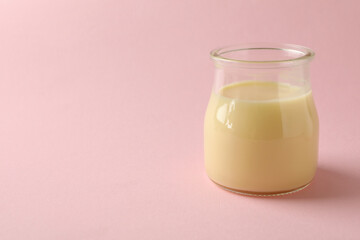 Glass jar with condensed milk on pink background
