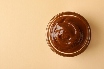 Glass bowl with caramel condensed milk on beige background