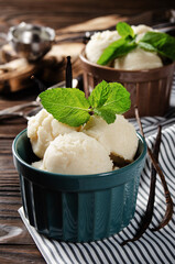 Vanilla icecream balls in clay bowls on wooden kitchen table with ice cream scoop aside