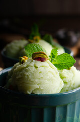 Pistachio icecream balls in clay bowls on wooden kitchen table with crumbs and nuts aside