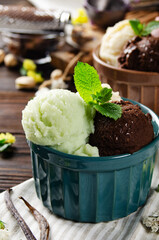 Three scoops of Vanilla pistachio and chocolate icecream balls in clay bowls on wooden kitchen table