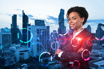 Successful smiling attractive black businesswoman pondering on technology at business process to achieve tremendous growth for client. Tech hologram icons over Bangkok background