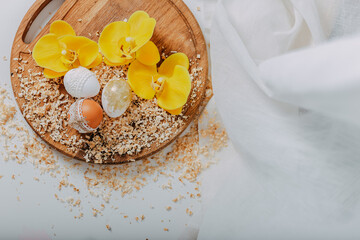 Three easter eggs with yellow orchid flowers on wooden background with sawdust around. Easter eggs with lace border on wooden cutting board. Eggs decoration. Golden easter egg with glitters.