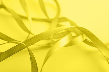 Curved yellow gold silk ribbon on yellow background. Closeup. Trendy color. Color 2021.