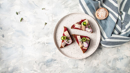Traditional matie herring with beetroot salad, fresh cucumber and onion rings on the toasts on white plate. Scandinavian cuisine