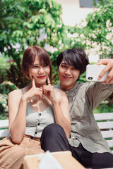 Lovely asian couple having romantic moment at park taking selfie with smartphone.