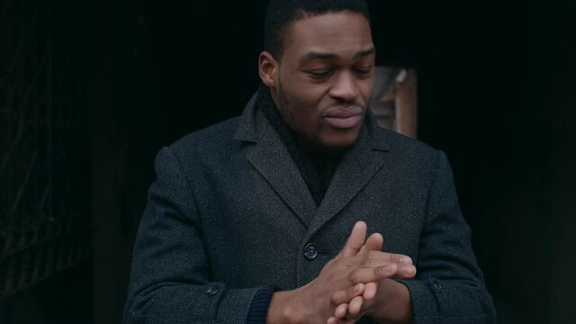 Young african american guy feeling cold, warming his hands outside on winter day, tracking shot