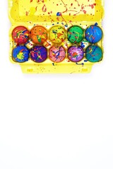 Bright Easter eggs painted with gouache in yellow egg box isolated on white background, top view copy space, vertical image 
