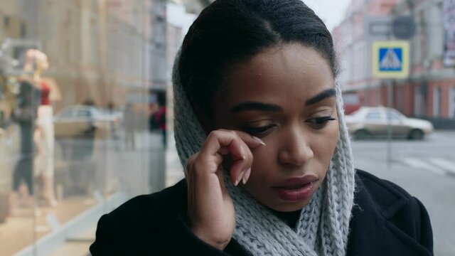 Close up portrait of young depressed black woman crying near shopping mall, no money for purchases, tracking shot