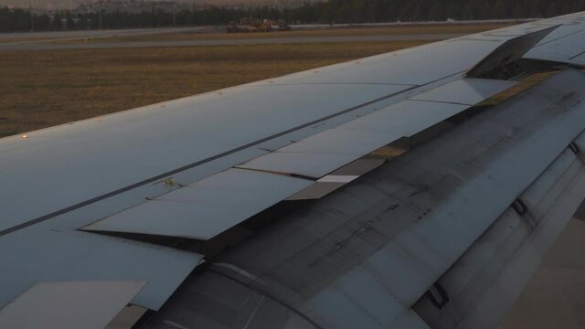 Powerful passenger airplane lowers flaps landing on flat runway of contemporary airport at summer sunset time extreme close view through window.