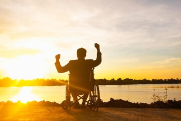 Silhouette young disabled man seeing river background.He is raise a hand to and sitting on wheelchair.despair,lonely,hope.Photo concept depression and Patient.