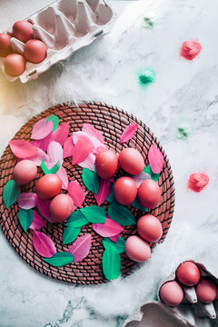 Colorful Easter composition of the chicken eggs, colored birds feathers, dyes for eggs on the marble table. Preparing for the easter holiday. Top view, flat lay image with festive atmosphere.