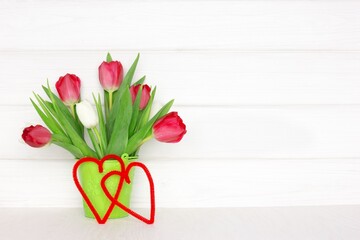Tulip flower bouquet with two hearts on wooden table near white wood wall. Valentine Day concept with copy space. Spring rustic background