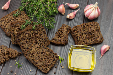 Pieces of black bread, thyme sprigs, butter in glass bowl and garlic on table