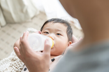 リビングで親に抱っこされてミルクを飲んでいる赤ちゃん