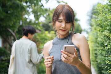 Asian thai woman jogging at park and looking at music playlist on smartphone.