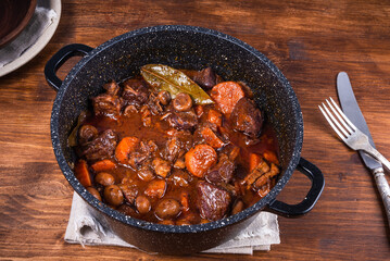 Ready burgundy beef in a saucepan on a wooden table close-up - top view