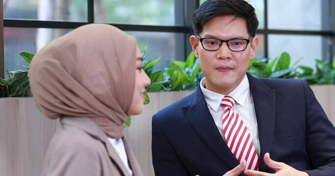Young business muslim woman and business man colleague walking and discussing outside the office. Woman is holding a coffee and businessman is holding a digital tablet outdoor.