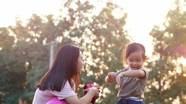 Young mother helps her daughter remove protective elbow pad after learning to ride scooter in summer park. Active outdoor sport for kids.