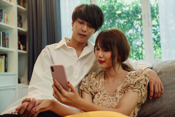 Asian thai couple holding hand checking wedding program on smartphone at living room.