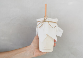 Woman hand is holding coffee cup with straw made from sugar product on gray background.