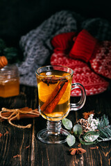 Glass cup of hot ginger tea with lemon and honey on dark wooden table. Sliced lemons on a chopping stone board