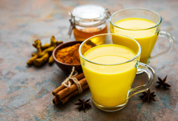 Yellow turmeric latte drink. Golden milk with cinnamon, turmeric, ginger  and honey over concrete background.
