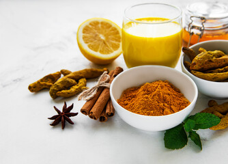 Yellow turmeric latte drink. Golden milk with cinnamon, turmeric, ginger  and honey over white marble background.