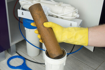 Plumber in yellow household gloves changes water filters. Repairman installing water filter...