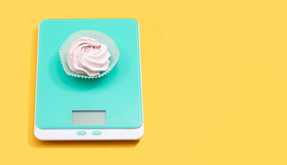 Marshmallow on electronic scales on a yellow background with space for text.