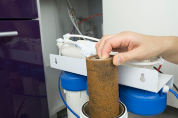 Close-up plumber hand holding used dirty rusty first-stage filter for drinking water. Changing...