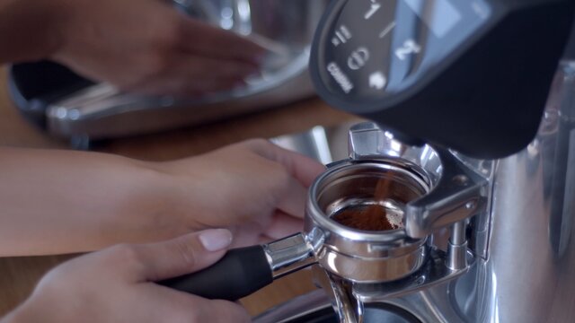 Caucasian white woman's barista hand inserting double portafilter in the grinder to collect fresh ground specialty coffee to make espresso. Professional grinder. High-quality jpg image close-up