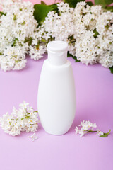 Fototapeta na wymiar Skin care products (tonic or lotion, serum, cream, micellar water, sea salt, cotton pads) on purple background with spring white lilac blossom. Freshness natural hair care. Shampoo and conditioner