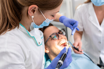 Female dentist with an assistant polishes teeth to a male patient in the dental clinic.